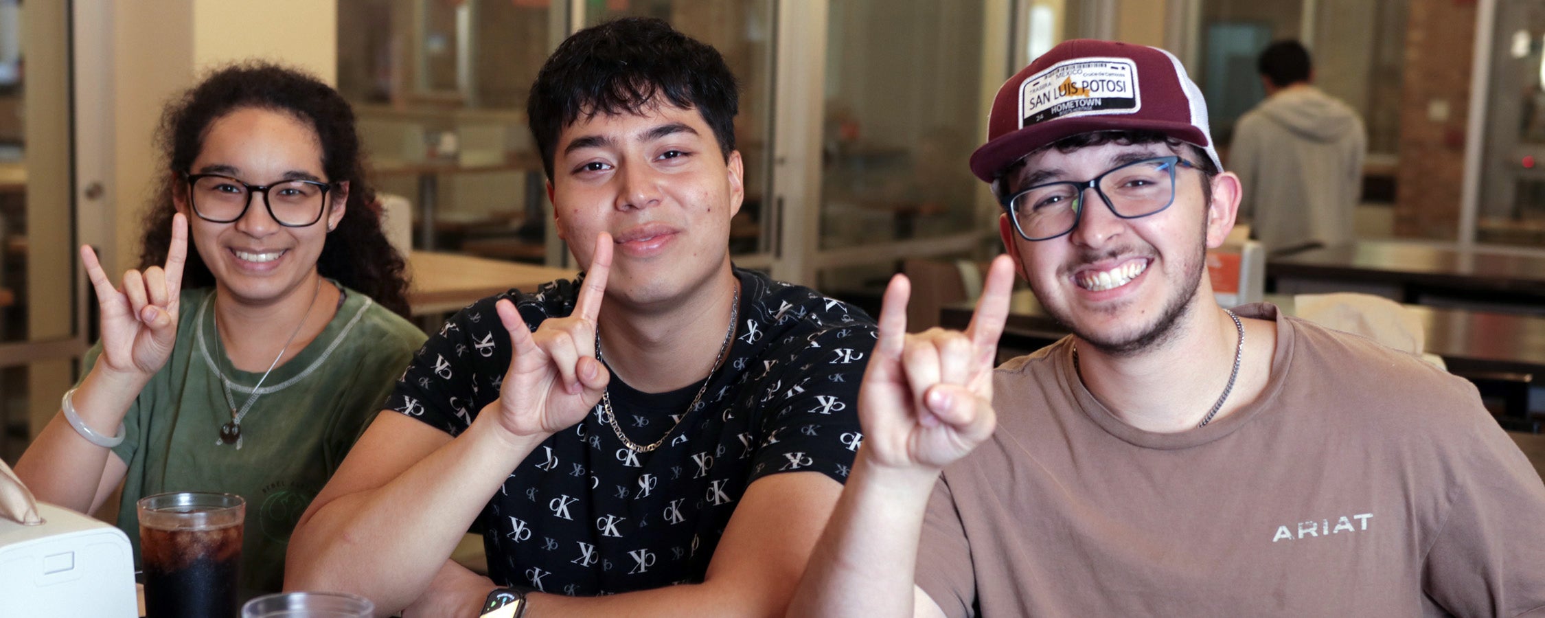 Three UT students pose together and make the Hook 'Em hand sign at J2 Dining.